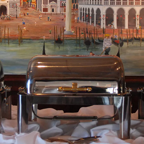 Chafing dish at a Mezza Luna buffet in front of a Venetian mural
