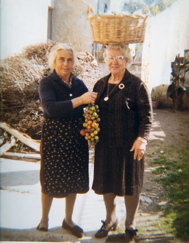 Two women carrying a basket and a string of tomatoes